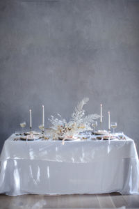 A minimalist, modern, neutral holiday tablescape for Christmas and your winter table setting with a natural, unique dried flower centerpiece, white linen table cloth, mini bouquet place settings, and brass gold flatware. It’s an elegant floral design, a DIY arrangement and homemade wreaths using pampas grass, bleached fern, tallow berry, bunny tail grass, and lunaria. Discover an organic, asymmetrical wreath tutorial along with a DIY Christmas cracker / popper how to, and sustainable gift wrapping ideas of muslin, linen, and upcycled paper with hand dyed silk ribbons and dried flower boutonniere gift toppers that can be reused year after year. By Beth Kirby | Local Milk Blog.